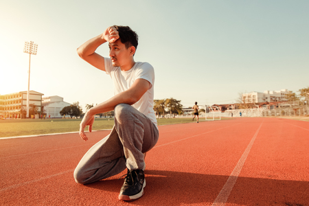 Tired wet athletic man wiping sweat his hand at sport stadium with sunset.の写真素材