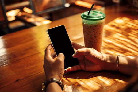 Hands use mobile phone near coffee on the table with light of sun.の写真素材