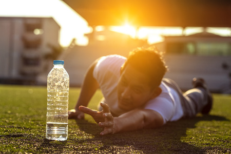 Thirsty man on grass at sport stadium reach for a bottle of pure water.の写真素材