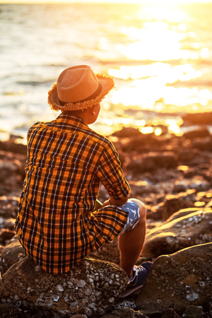 A man travel and  sitting on the stone near sea water and sunset in summer.の写真素材
