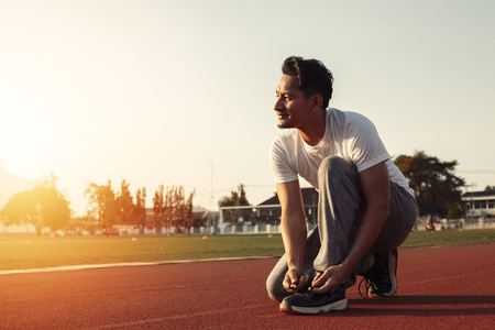 attractive brunette man enlacing him sport shoes on track race. A man at sport stadium with sunset.の写真素材
