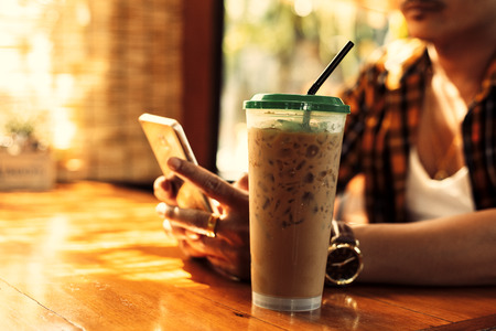 Ice coffee is on the table near hands use mobile phone at summer in coffee shop.の写真素材