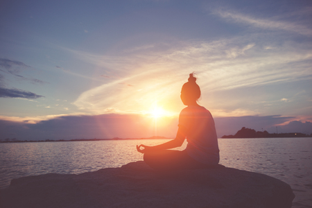 A women yoga on the rock near the sea with sunset sky.の写真素材