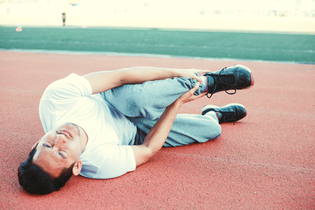 Twisted ankle. Young runner touching his sprained leg between jogger at sport stadium.の写真素材