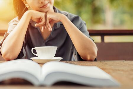teacup on wood table in front of woman smile and relaxing between read a book.の写真素材
