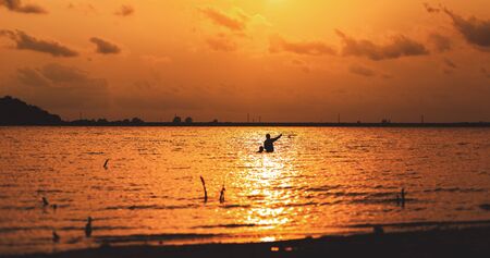 Two fisherman try catch a fish by trap in the water at sunset.の写真素材
