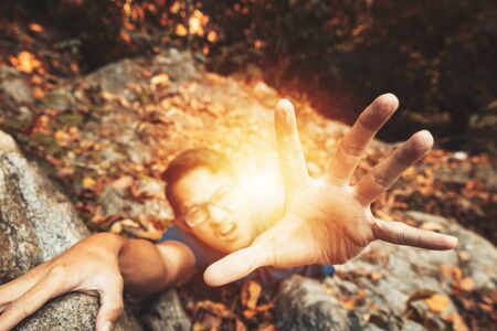 A man climb rock in the forest and hand for help.の写真素材