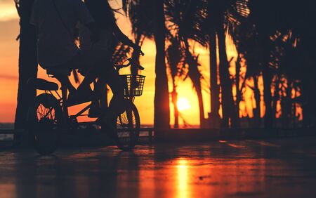 Couple ride bike on the road near the beach with sunset.の写真素材