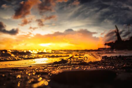Plastic water bottle on the beach, environment pollution. Dirty beach and sunset.の写真素材
