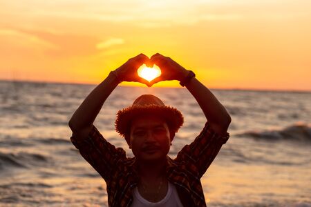 hands forming a heart shape with sunset on the beach.の写真素材