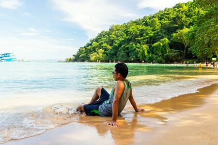A man sitting on the beach in sea water flow at island midday.の写真素材