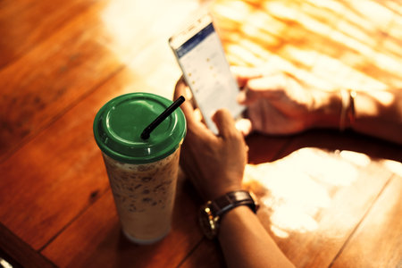 Ice coffee is on the table near hands use mobile phone at summer in coffee shop.