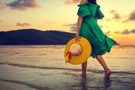 Woman walking on the beach in summer vacation wearing hat and dress enjoying the view at the island beach.の写真素材