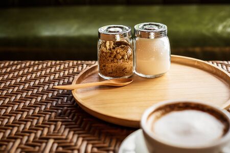 Sugar in pot on wood plate near cup of coffee.の写真素材
