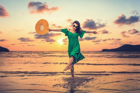 happy women hold hat and kick water splash on the beach at sunset. Vocation, Holiday at the beach.の写真素材