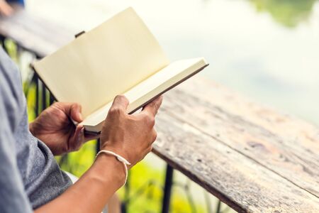 A man hold book and reading in the parks near the river.の写真素材
