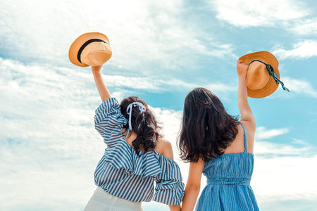 Two happy girl hold hat and raise arms in the sky. People traveling relaxing and enjoying  at...