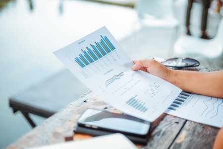 Businessman hold paper graph chart on the table near the river. Working at vocation.の写真素材