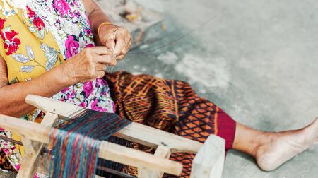 Old asian women hold silk of thread near rool of silk onthe ground.の写真素材