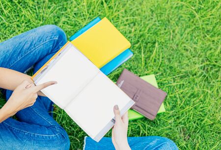 University students sit and read on the grass in the evening.
Hand point a book.の写真素材