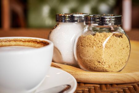 Sugar in pot on wood plate near cup of coffee.の写真素材