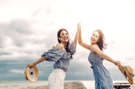 Two happy girl hold hat and raise arms in the sky. People traveling relaxing and enjoying  at summer.の写真素材