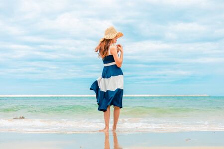 Happy Woman walking on the beach in summer vacation wearing hat and dress enjoying the view at the island beach.の写真素材