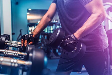 Sporty young man lifting a dumbbell in a gymの写真素材