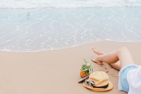 Women sitting on the beach and sea water flow. Hat, passport, pineapple near people.の写真素材
