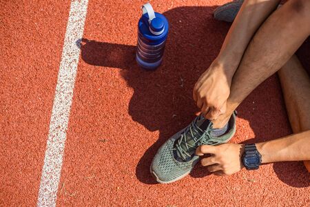 attractive brunette man tie their shoes before run on  track race. A man at sport stadium. water bottle on the ground near sport man.の写真素材
