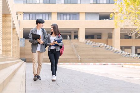 high school students hold book and laptop talking and laughing in a hallway between classesの写真素材