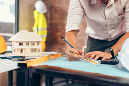 engineers holding a pen pointing to a building and  drawing outlay construction plan as guide for...