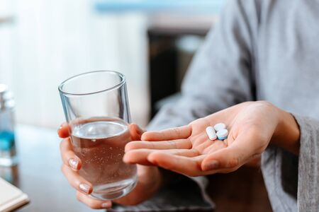 Businesswomen working at home with glass of water takes white round pill in hand.の写真素材