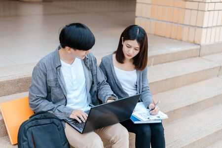 teenager sitting on stair at college campus with school books and a laptop computer doing homework.の写真素材