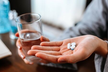 Businesswomen working at home with glass of water takes white round pill in hand.の写真素材