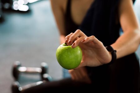 Woman exercise in gym fitness breaking and relax. hand  holding apple fruit after training sport and dumbbell, water bottle on the ground.の写真素材