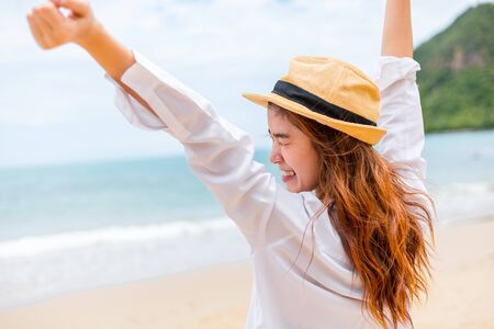 Woman raise hand up on the beach. Happy woman wearing hat.の写真素材