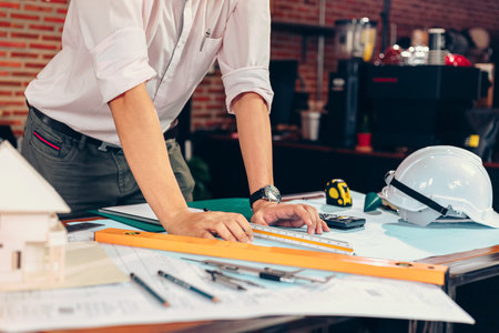 engineers holding a pen pointing to a building and  drawing outlay construction plan as guide for...