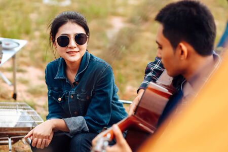 A man plays a guitar for a woman while camping beside the lake.の写真素材