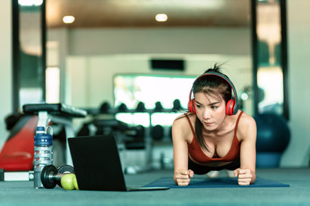 Full-length of young beautiful woman in sportswear doing plank at gym. Women and ear phone listen...
