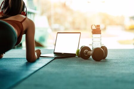 Full-length of young beautiful woman in sportswear doing plank at gym. Women and ear phone listen music between workout.の写真素材
