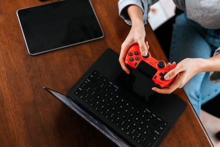 Funny Young woman wearing earphones playing computer game on laptop with joypad.