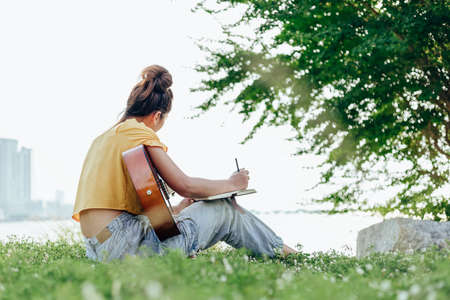 songwriter create and writing notes,lyrics in the book on grass at parks beside the sea and building city background.の写真素材
