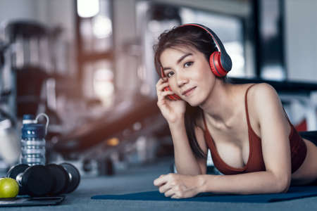 Women and ear phone listen music between workout and relaxing. Laptop, apple, dumbbell and water bottle on the ground beside people.の写真素材
