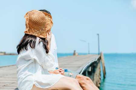 Honeymoon travel couple hugging and sitting on wood bridge and enjoys their tropical holiday. People love and romantic concept.の写真素材