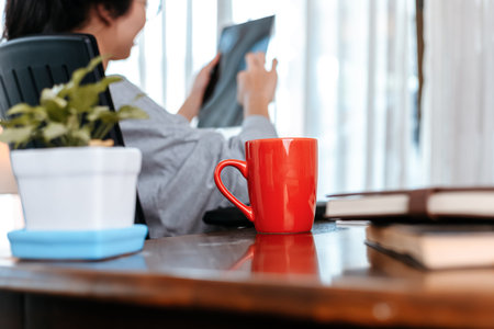 woman working on laptop and hold cup of coffee while sitting at working place.