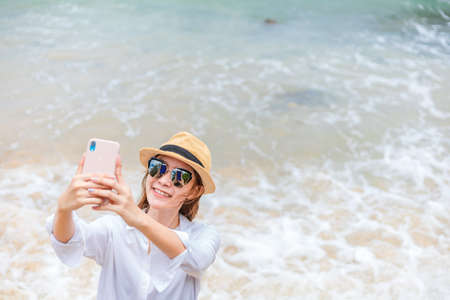 Happy young women wearing  sun glasses use mobile phones to take pictures on the beach While traveling.の写真素材