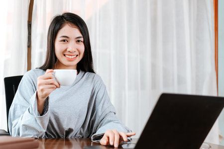 woman working on laptop and hold cup of coffee while sitting at working place.