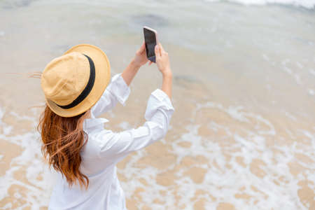 Happy young women wearing  sun glasses use mobile phones to take pictures on the beach While traveling.の写真素材