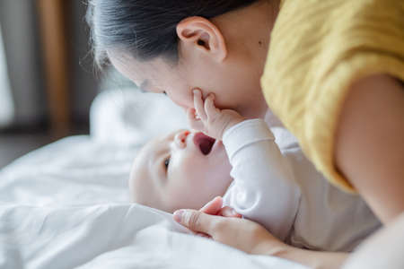 Happy Mother kiss and playing with cute baby at house. Family love and care. Family infant, newborn concept.の写真素材